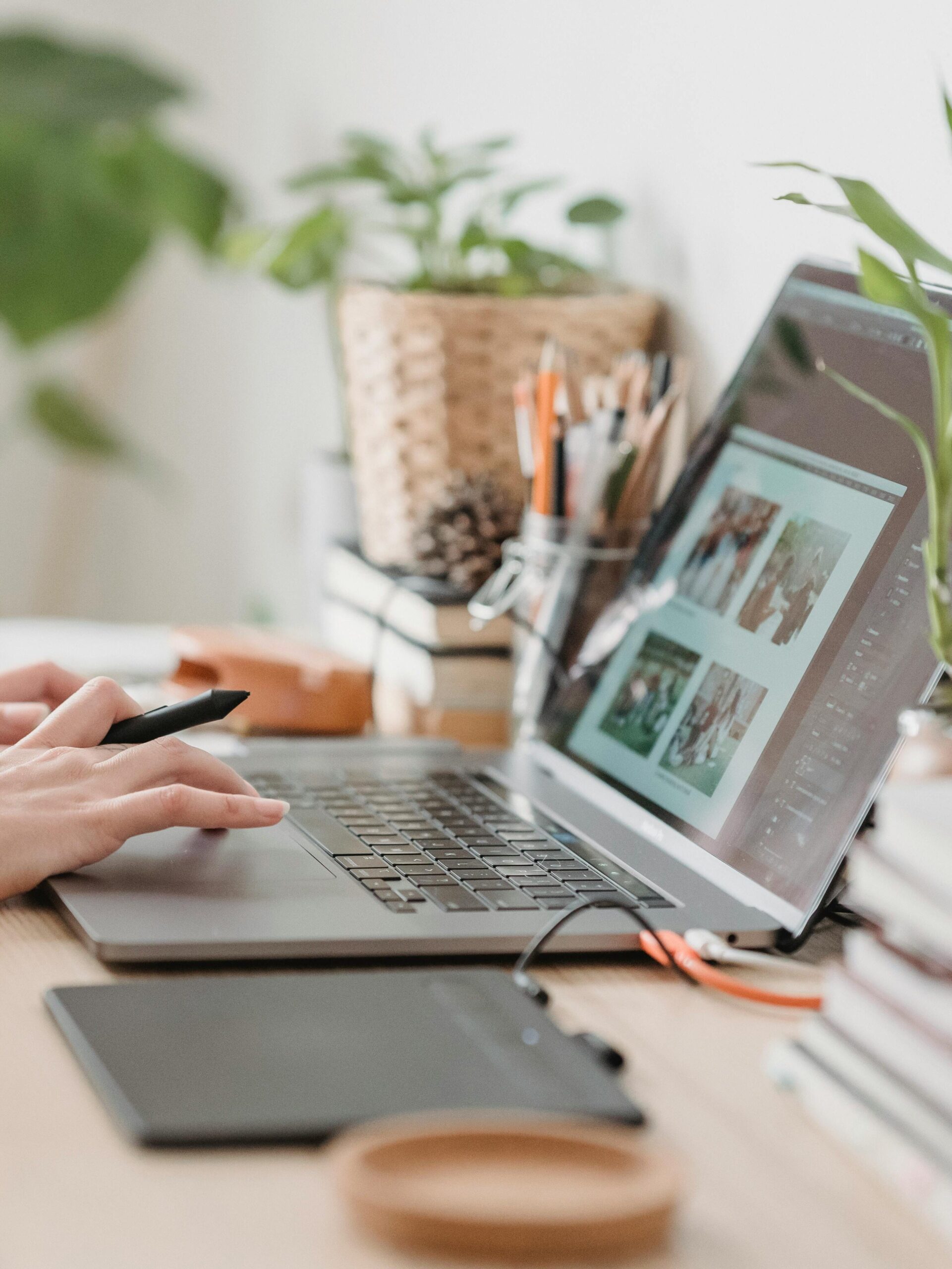 Freelance designer working from home using a laptop and digital tablet, surrounded by plants.